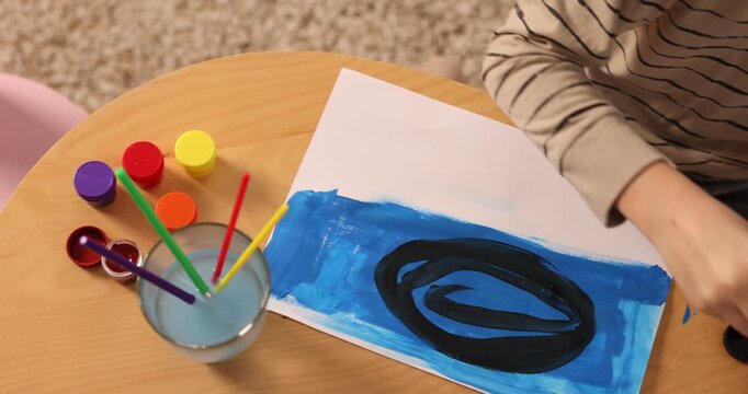 Little boy drawing with brush and paints at wooden table, top view. Camera moving left