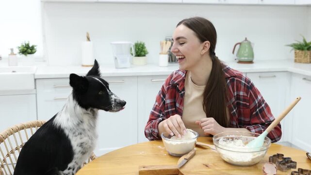 Woman making cookies near cute dog at wooden table in kitchen