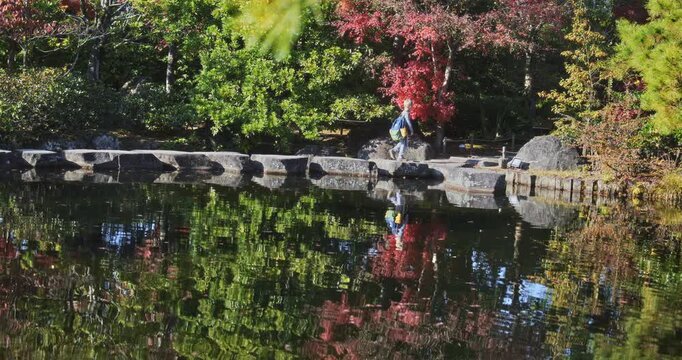 Panning shot of little boy walking past beautiful, still pond with surrounding autumn trees