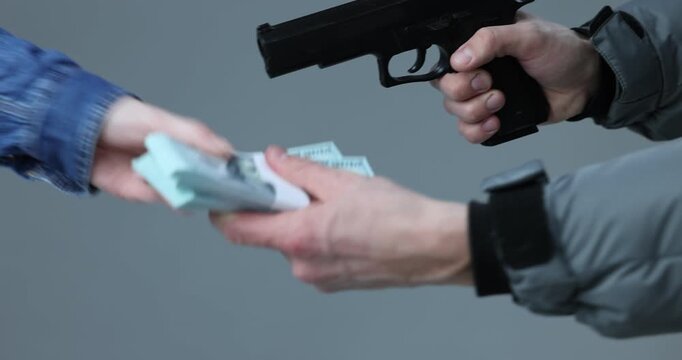 Woman giving money to dangerous criminal with gun on grey background, closeup. Armed robbery