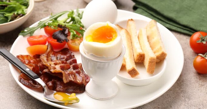 Tasty breakfast with soft boiled eggs and bacon served on grey table, closeup. Camera moving in