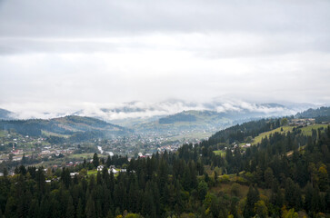 Fototapeta premium Tranquil mountain Verkhovyna village tucked in a green valley with scattered homes and rolling hills. Overcast skies create a calm, scenic mood. Carpathian Mountains, Ukraine