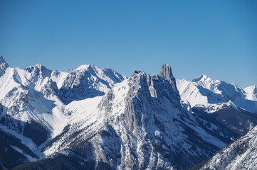 Obraz premium Close-up of rugged snow-covered mountain peaks against a clear blue sky in winter.