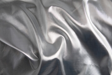 Elegant silver satin fabric with soft flowing folds and reflective metallic sheen, styled as a festive holiday background. The luminous texture and cool winter tones create a luxurious seasonal backdr