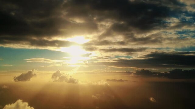 Sunlight breaks through clouds at dawn, illuminating the sky with golden rays and creating a serene atmosphere over the horizon in a breathtaking aerial view