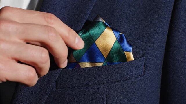 Close-up of a man's hand adjusting a colorful silk pocket square in his navy blue suit jacket