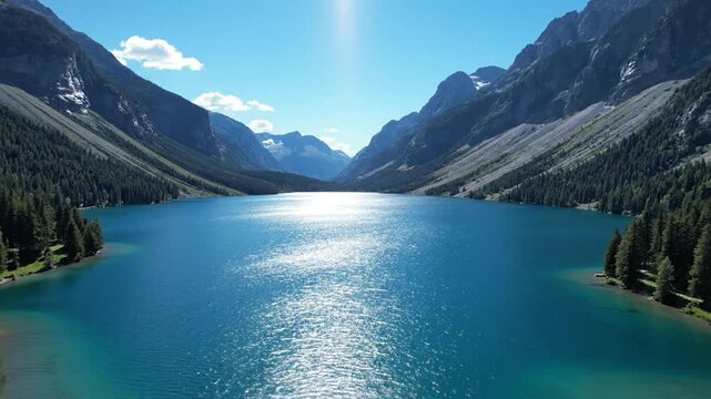 Sunlight glimmers on a mountain lake surrounded by lush green forests.