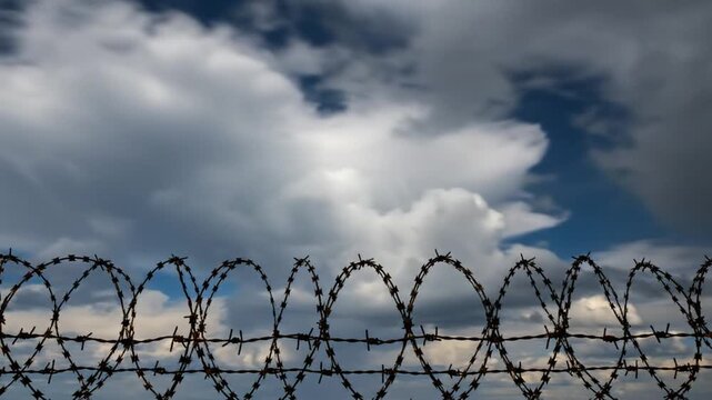 Barbed wire security fence with dark clouds and blue sky in background creating a sense of confinement and protection