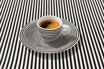 A striped cup of dark coffee sits on a matching striped saucer