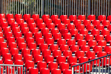 Rows of bright red plastic chairs form a striking grid on tiered metal platforms. The empty seats and railings create a bold, orderly architectural pattern