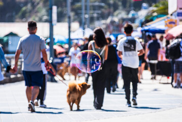 Close-up of a floating soap bubble against a bright coastal background with blurred people walking along the promenade. Sunny seaside atmosphere in San Antonio, Chile.