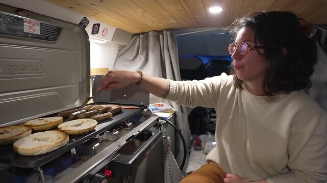 Woman cooking sausages and bagels in camper van