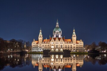 Fototapeta premium Explore Hannover, Germany, and witness the New Town Hall glowing at night. Its reflection dances on the Maschsee lake, showcasing the city s architectural beauty and charm.