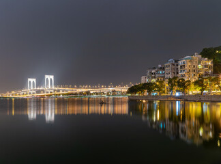 Fototapeta premium Illuminated bridge and cityscape reflected in calm water at night.