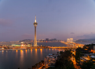 Obraz premium Macau tower and bridges glow at twilight over harbor waters.
