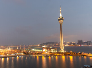 Fototapeta premium Macau tower illuminated at dusk over waterfront cityscape.