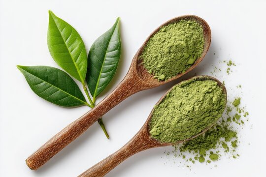 Two wooden spoons overflowing with vibrant green powder, near fresh tea leaves