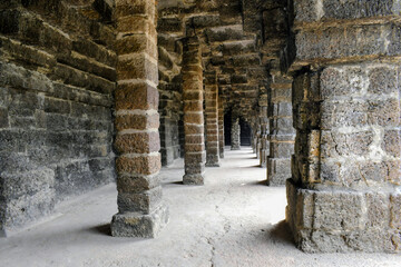 Obraz premium a deep perspective view of the interior corridor at kurumbera fort, showcasing rows of massive, rectangular laterite pillars and the intricate block masonry used in medieval indian structural engineer