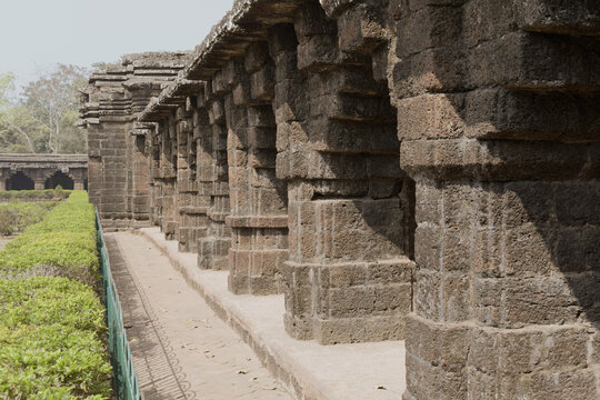 ancient kurumbera fort corridor in west bengal, showing a row of historic carved stone pillars and arches made of weathered laterite blocks under bright daylight