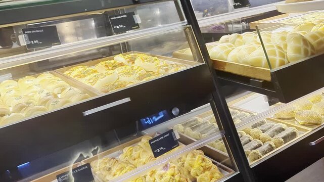 Freshly baked bread, buns, and pizza displayed inside a modern glass showcase at a bakery shop.