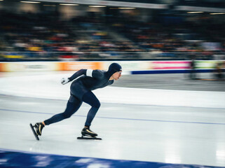 スピードスケート選手の疾走。屋内リンクでのダイナミックな流し撮り（モーションブラー）、ウィンタースポーツ競技