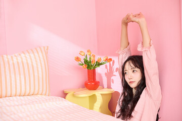 ピンク背景の部屋でリラックスするアジアの若い女性のポートレート