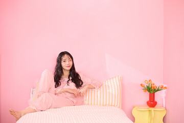 ピンク背景の部屋でリラックスするアジアの若い女性のポートレート