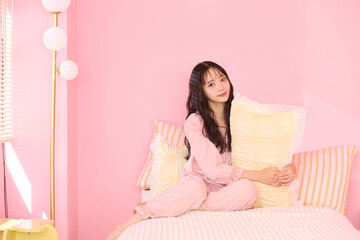 ピンク背景の部屋でリラックスするアジアの若い女性のポートレート
