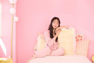 ピンク背景の部屋でリラックスするアジアの若い女性のポートレート