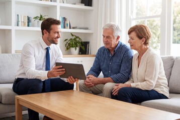 Smiling financial advisor showing tablet to senior couple during home consultation meeting