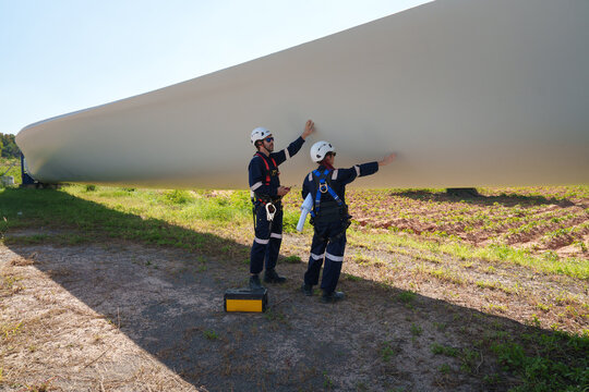 An engineer carefully examines a wind turbine blade at a construction site, placing a large blade on the ground to highlight the renewable energy technology.