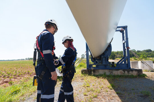 Engineers in safety gear conduct a detailed inspection of wind turbine blades at a construction site. Large blades are placed on the ground, highlighting the renewable energy technology.