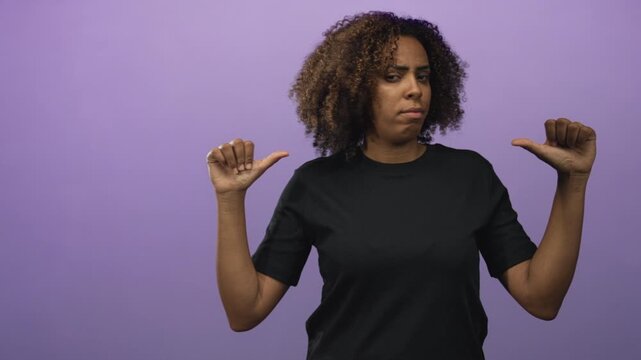 Woman wearing black t shirt pointing thumbs at herself in a purple studio; self identity empowerment skeptical.