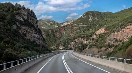 Winding mountain road with asphalt curves leading to a majestic rocky peak under a blue sky. Beautiful scenic landscape for travel and adventure concepts