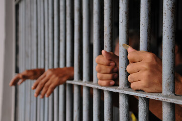Obraz premium hands of a prisoner behind prison bars on black background