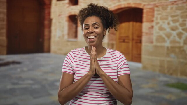 Woman presses hands together in prayer with closed eyes on an old town stone street in front of a building; gratitude prayer.