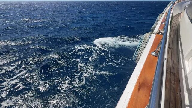 Side deck view with waves hitting floating yacht hull in blue sea