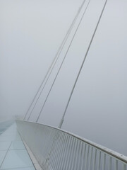 Yuntiandu glass bridge over Zhangjiajie Grand Canyon with row of cables shrouded in morning fog