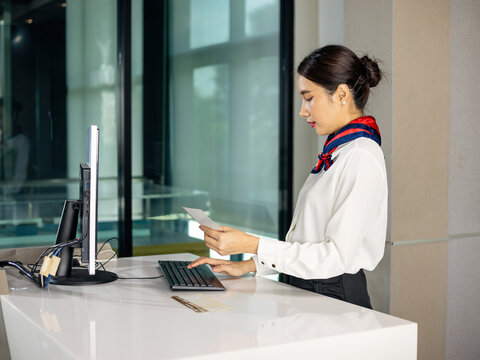 Professional Airline check-in counter staff working and holding document at reception desk in airport, corporate administration, customer service concept