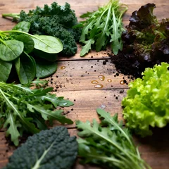 A variety of fresh leafy greens arranged on a rustic wooden surface. The assortment includes spinach , kale, arugula, and different lettuce varieties. © Pornrapat