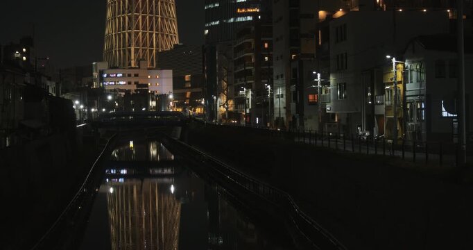 Medium shot of still water in canal flowing through Japanese city at night