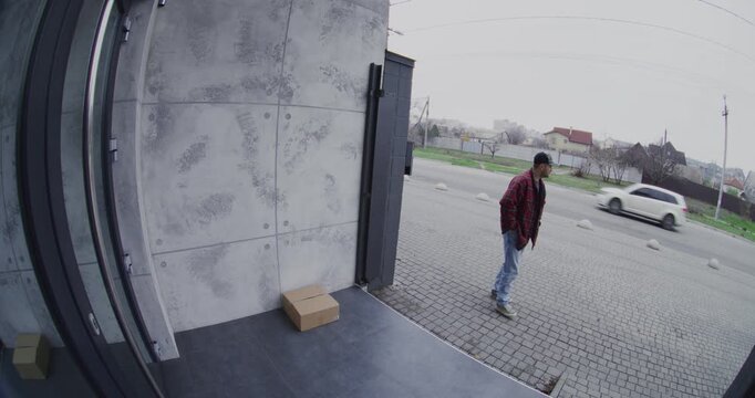 Man in Plaid Shirt Walking Past House Notices Large Package on Porch. Male Robber Quickly Grabs Box and Flees Scene, Captured by Smart Doorbell Camera. Concept of Home Mail Theft and Security Risks.