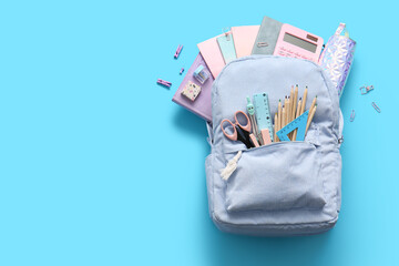 Blue school backpack with different stationery supplies on color background