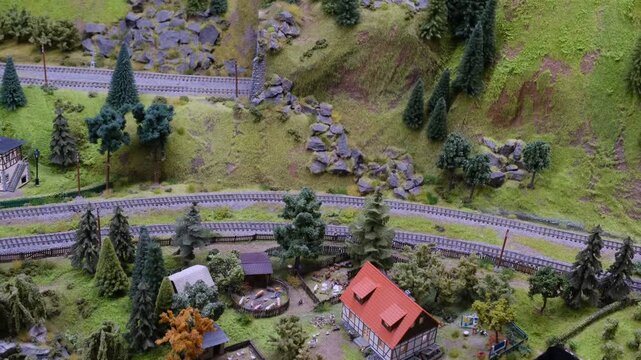 a detailed and colorful model train layout depicting a small railway yard surrounded by lush greenery and trees, at a realistic, miniature scale, that creates a whimsical atmosphere