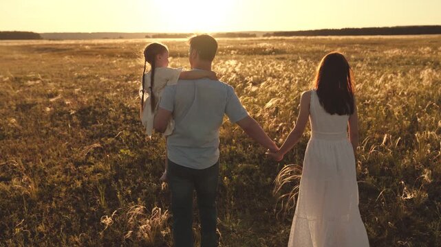 Father carries daughter blending with rustle of wind through ears of wheat. Father embraces held daughter and wife walks near wheat field. Father holds daughter in arms remained unwavering