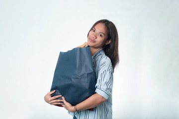 Fototapeta premium A young Indonesian woman looking content while hugging her shopping bags. Concept for retail therapy, consumer satisfaction, and successful shopping.