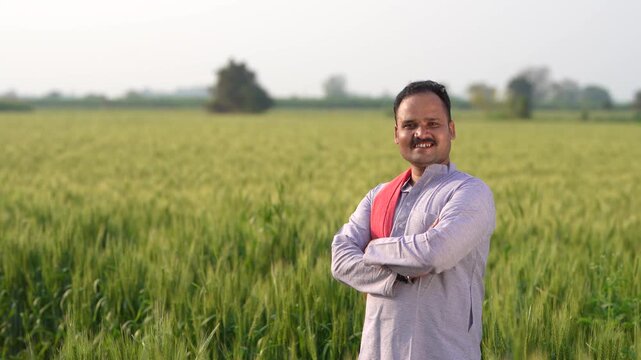young indian farmer standing at green wheat field