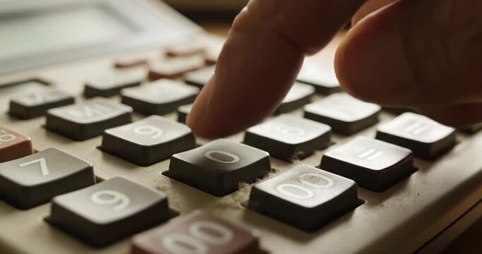 Close-up of a hand pressing the zero key on an old calculator with a blurred background