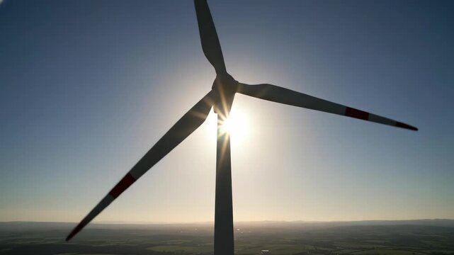Silhouette of a wind turbine against a bright sun and blue sky.