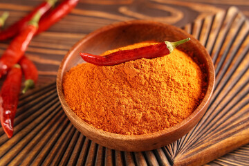 Bowl with red chili powder and peppers on wooden background, closeup